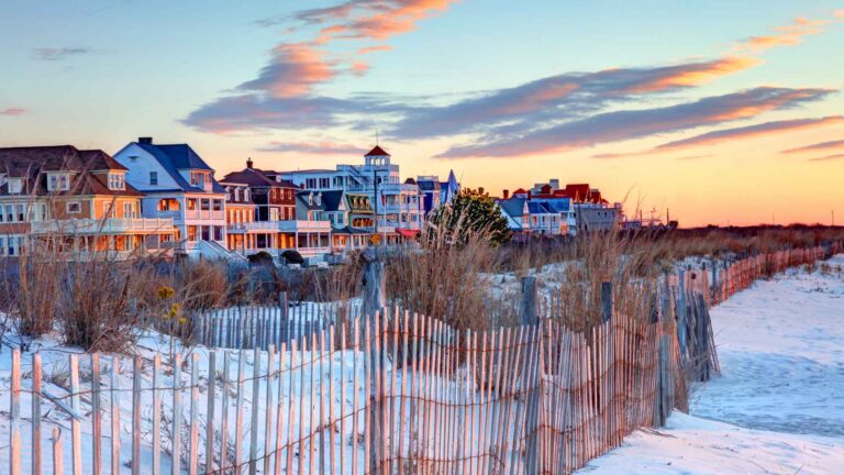 Snow-covered beach houses and dune fencing beneath a colorful winter sunset