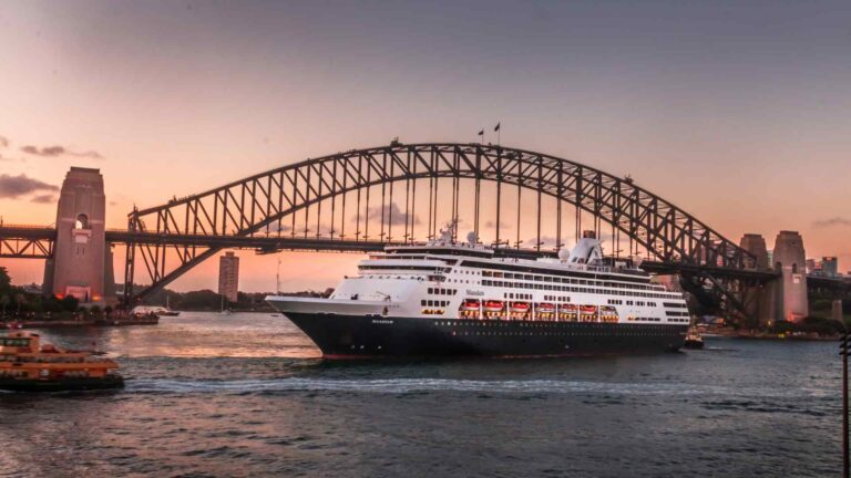 Cruise ship sailing beneath the Sydney Harbour Bridge at sunset