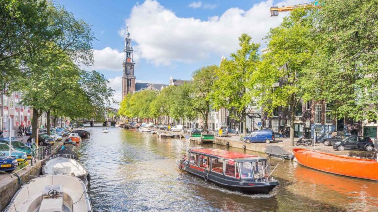 Amsterdam canal lined with boats, trees, and historic buildings