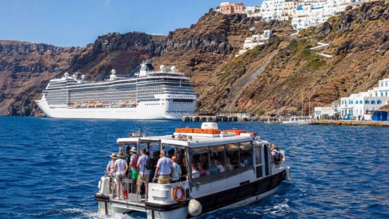 Cruise tender carrying passengers across Santorini’s blue caldera toward the island, with a cruise ship and whitewashed cliffside buildings in the background.