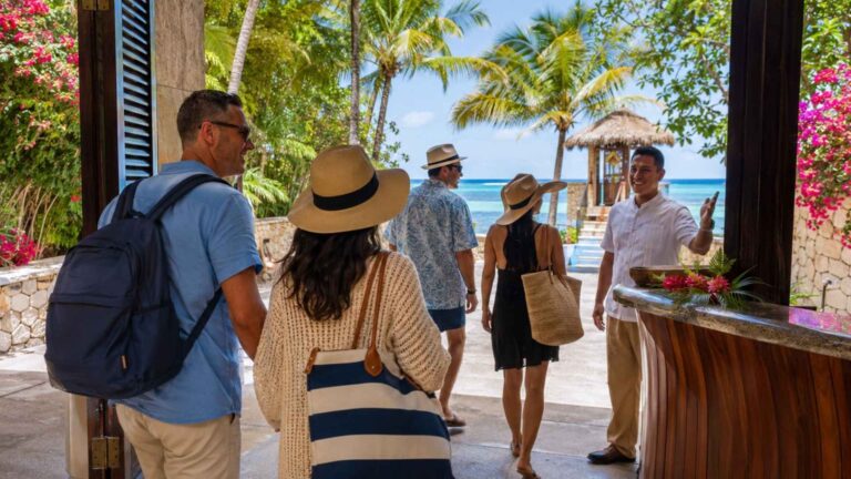 Cruise guests entering a tropical beach resort lobby near port while a staff member welcomes them toward the oceanfront property.