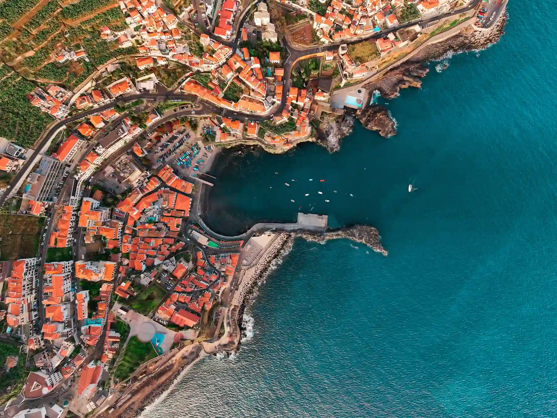 Aerial view of a coastal harbor and red-roofed waterfront neighborhoods near Funchal, Madeira.