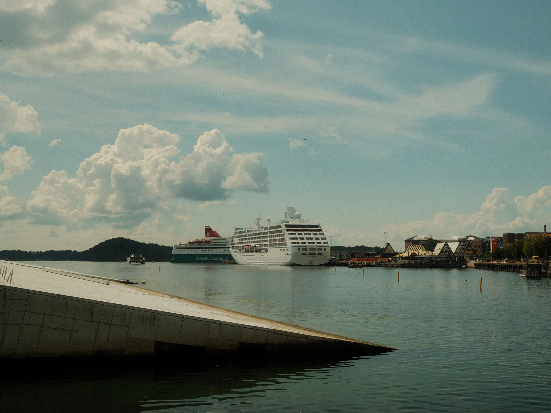 Cruise ships docked in Oslo harbor beside the city waterfront under summer clouds.