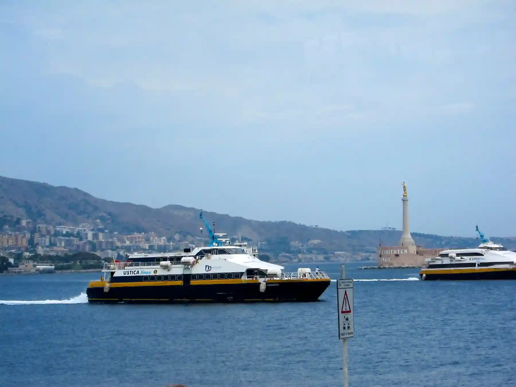 Passenger ferry crossing Messina harbor with the Madonna della Lettera monument behind it.