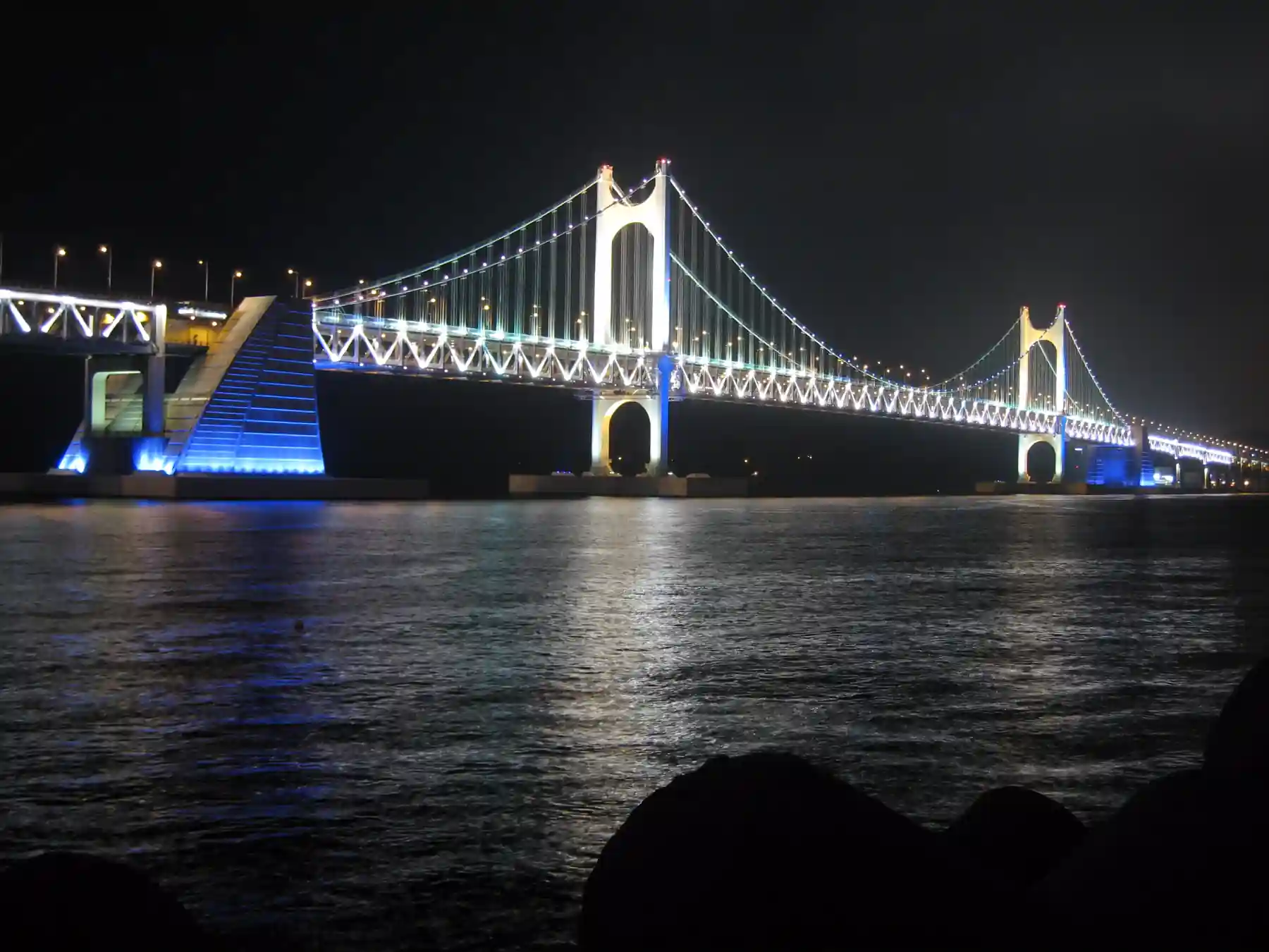 Gwangandaegyo Bridge illuminated over the water in Busan at night.