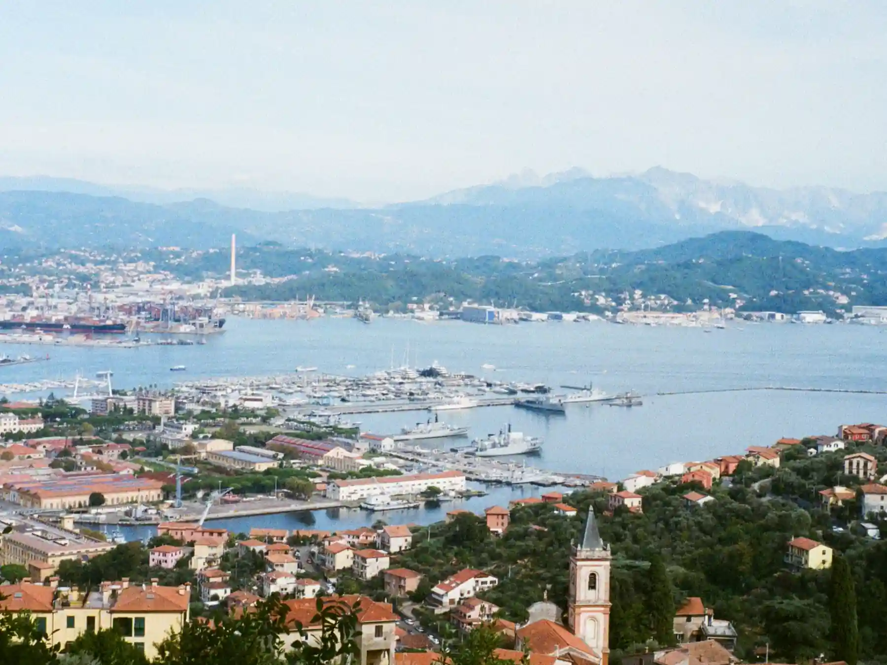 Elevated view of La Spezia harbor and naval waterfront with mountains behind the city.