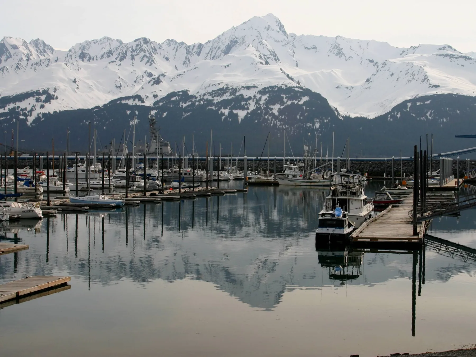 Boats and docks reflected in Seward Harbor beneath snow-covered mountains.