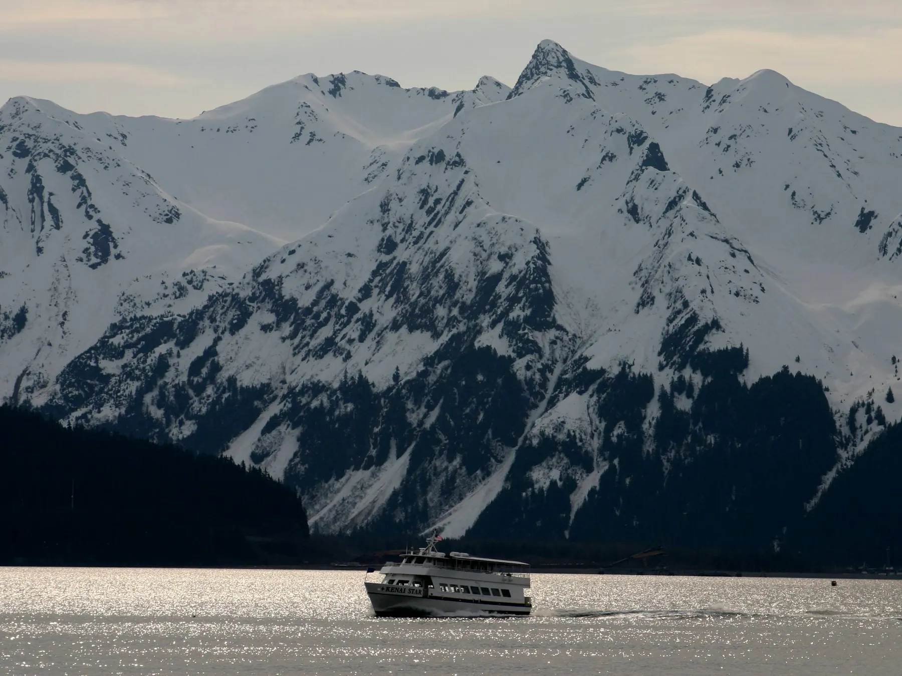 Tour boat crossing Resurrection Bay beneath steep snow-covered mountains near Seward.