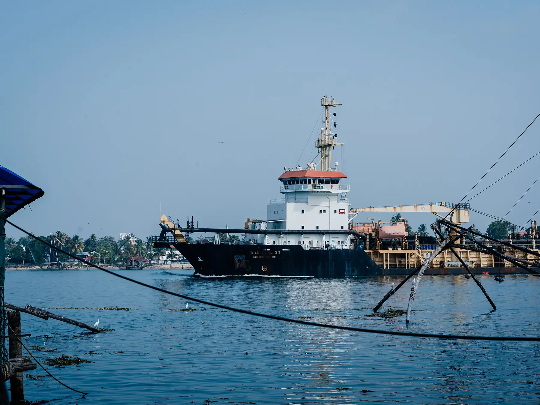 Cargo ship passing traditional Chinese fishing nets in Kochi harbor