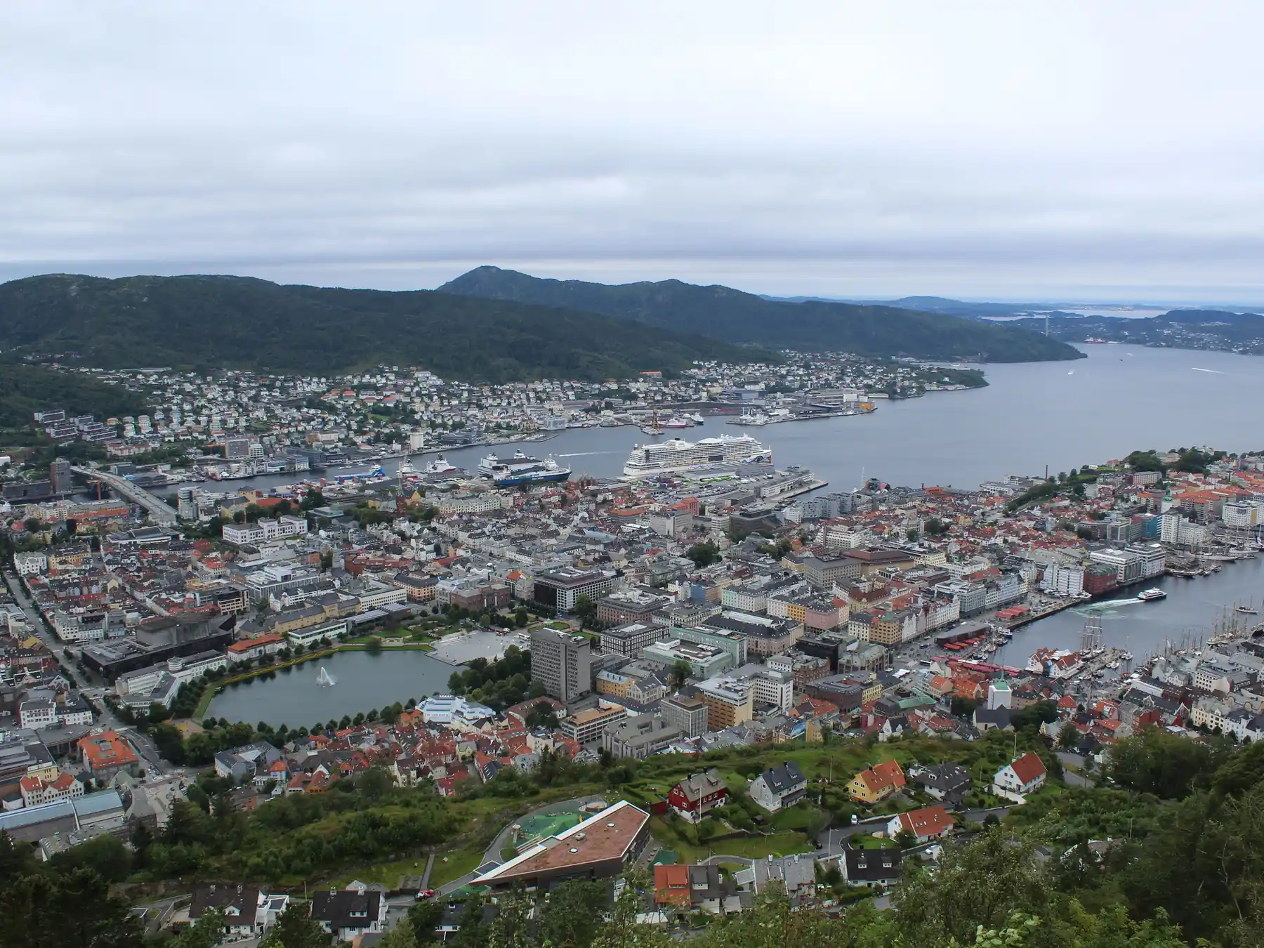 Wide aerial view of Bergen harbor, fjord, city, and surrounding mountains.