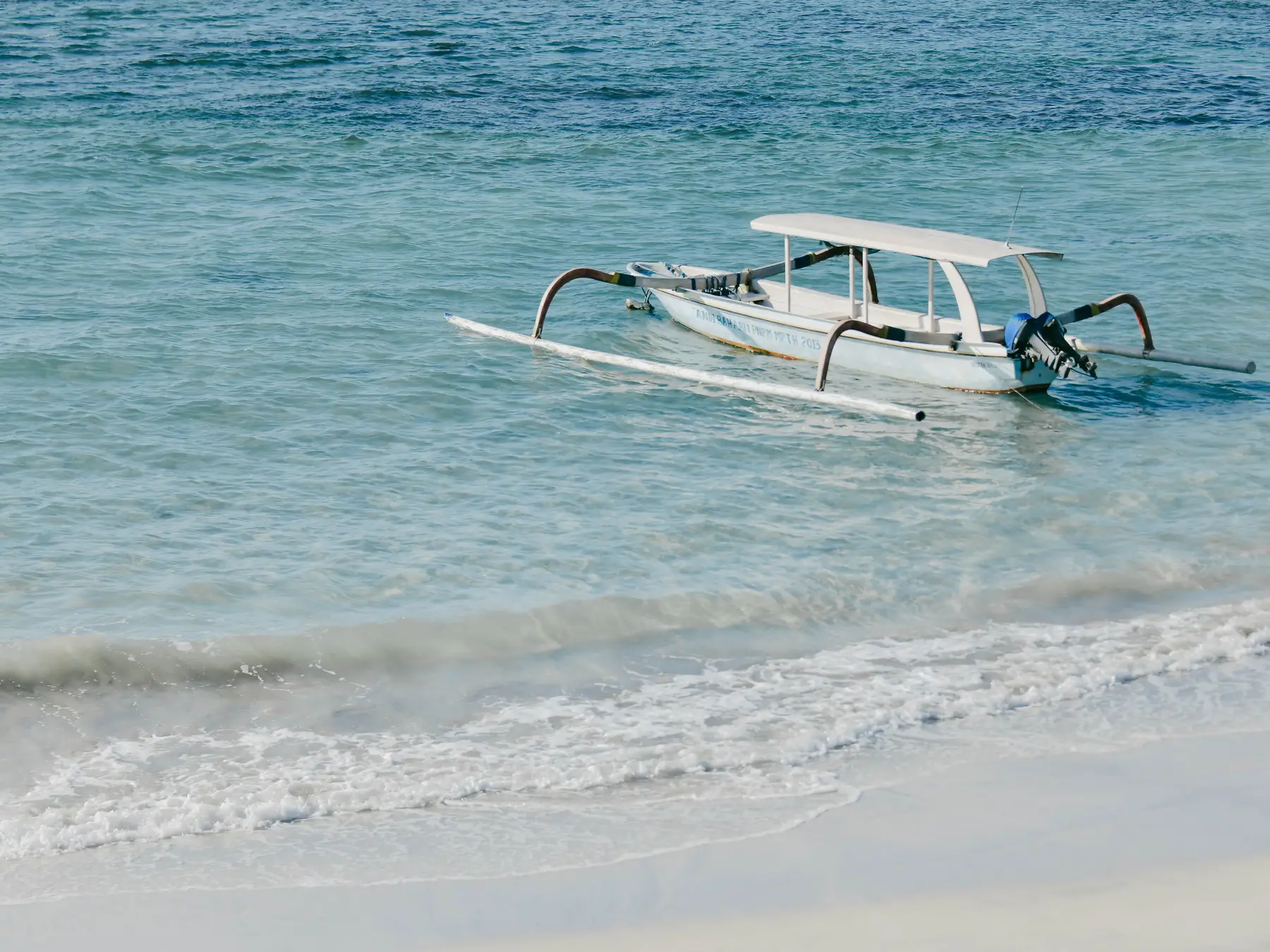 Traditional Balinese wooden boat anchored in clear blue coastal water.