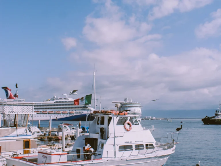 Yacht with a Mexican flag in Ensenada harbor with cruise ships behind it.