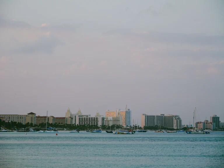 Boats and waterfront buildings in Oranjestad harbor beneath a pastel twilight sky.