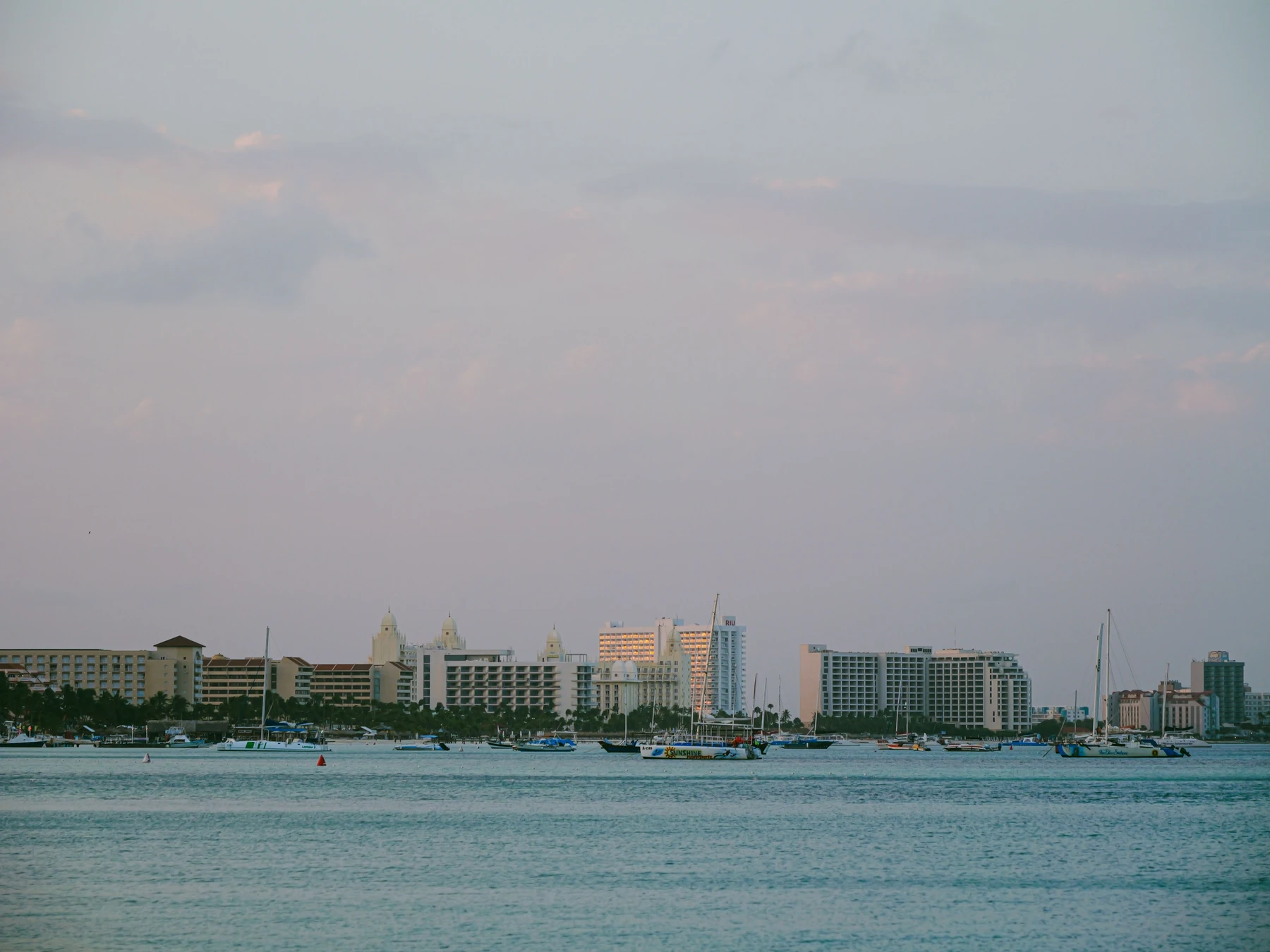 Boats and waterfront buildings in Oranjestad harbor beneath a pastel twilight sky.