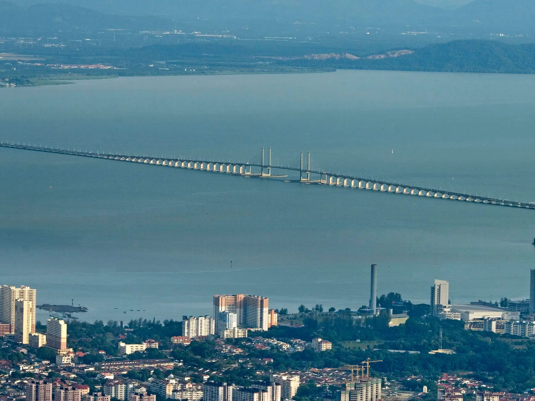 Aerial view of Penang Bridge stretching across the water beside the city.