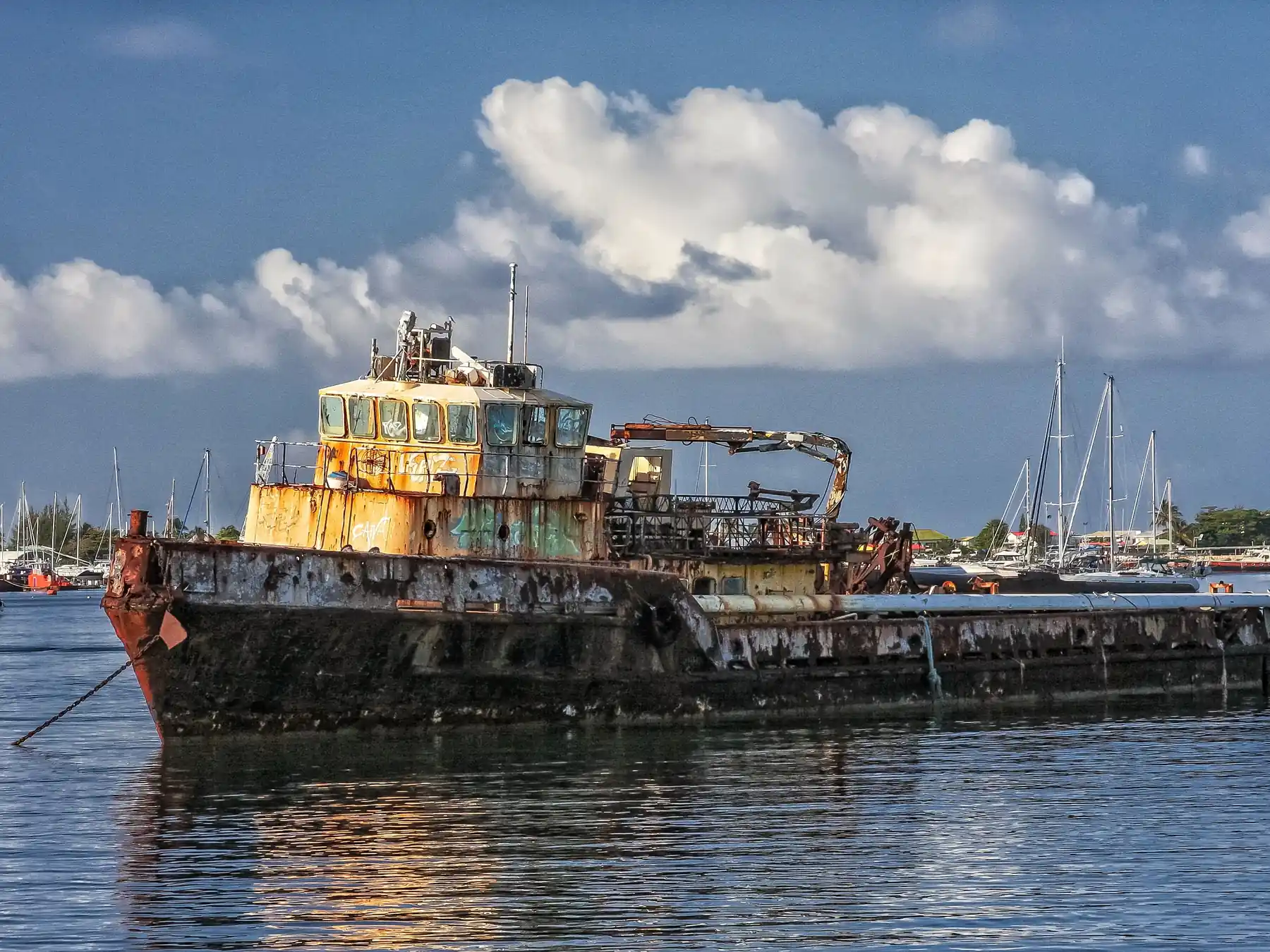 Weathered barge and sailboats floating in a Sint Maarten harbor.