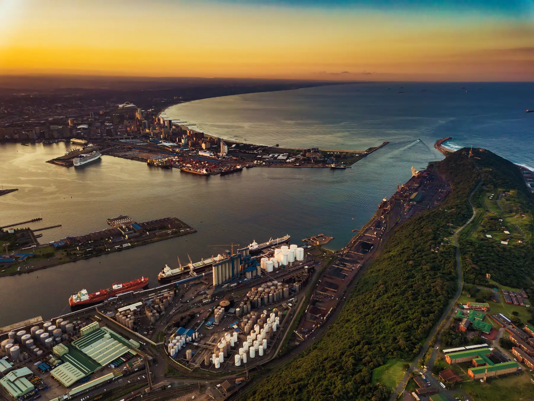Aerial view of Durban harbor, port channels, and city skyline at sunset.