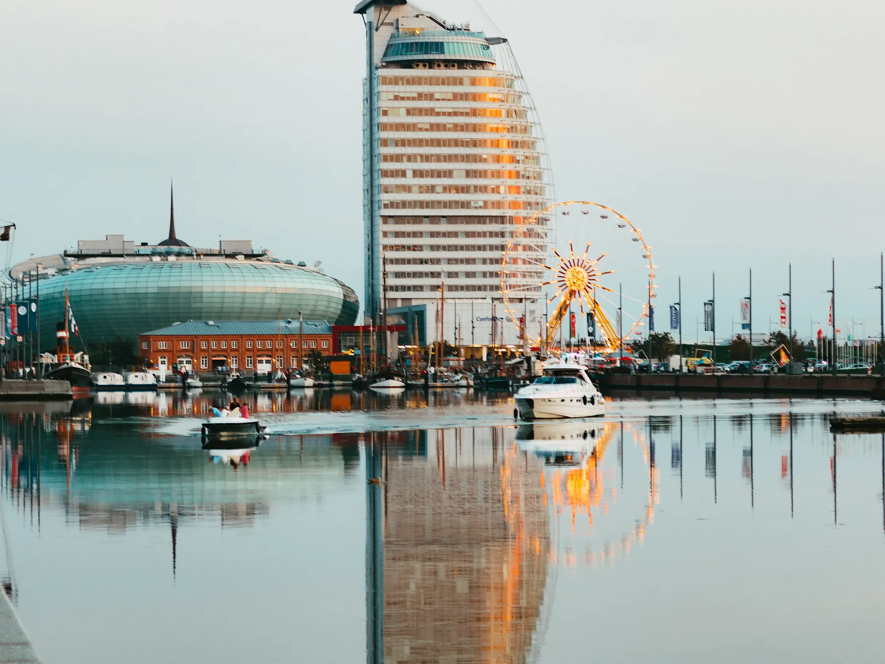Ferris wheel and modern waterfront buildings reflected in Bremerhaven harbor.