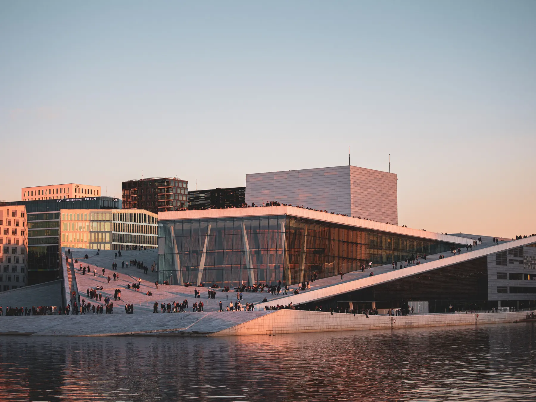 Oslo Opera House glowing at sunset beside the calm harbor waterfront.