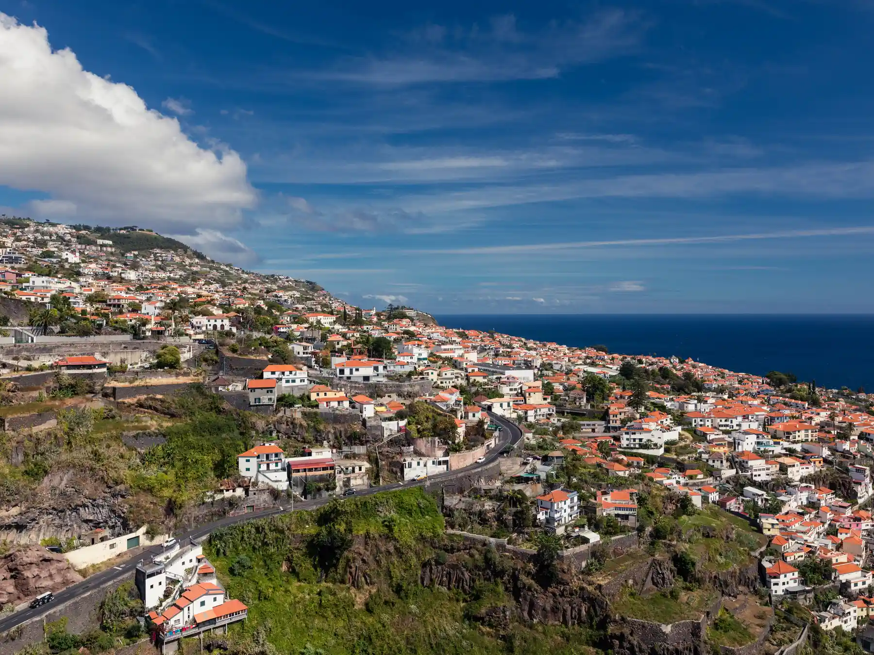 Red-roofed homes on the green hillsides of Funchal overlooking the Atlantic Ocean.