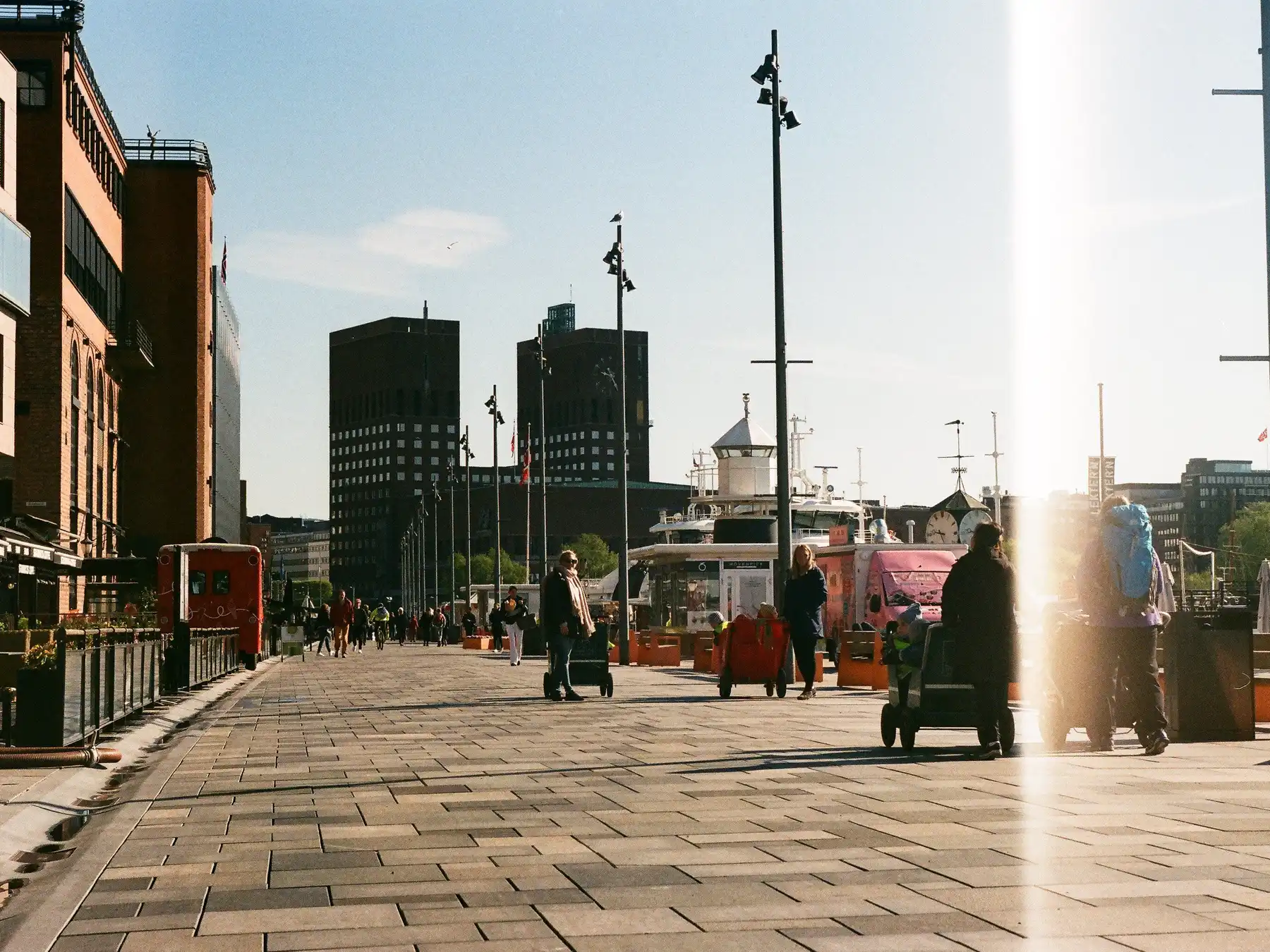 People walking along the Oslo waterfront with City Hall and harbor boats ahead.