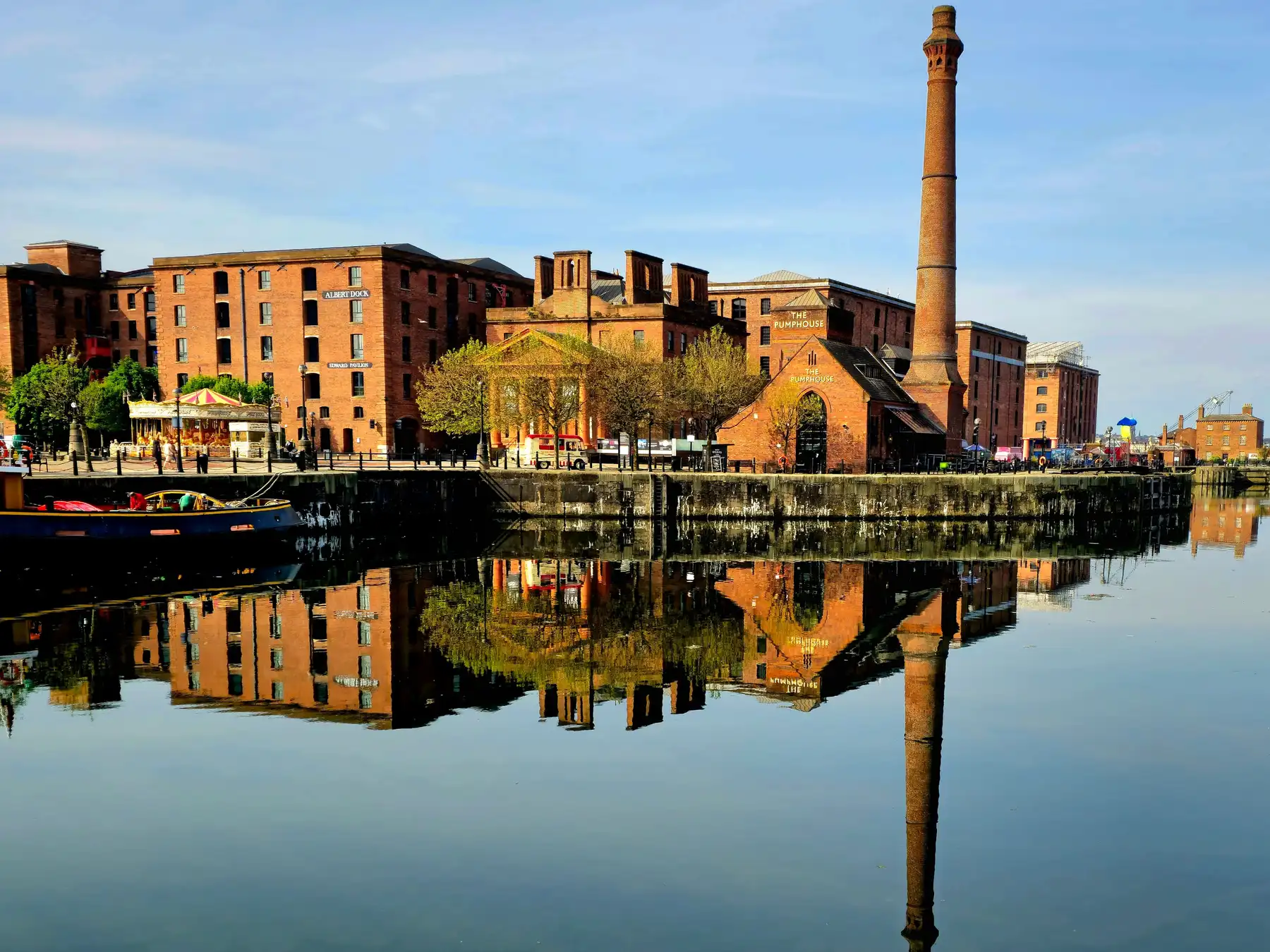 Red-brick warehouses and chimney at Liverpool’s Royal Albert Dock reflected in calm water.
