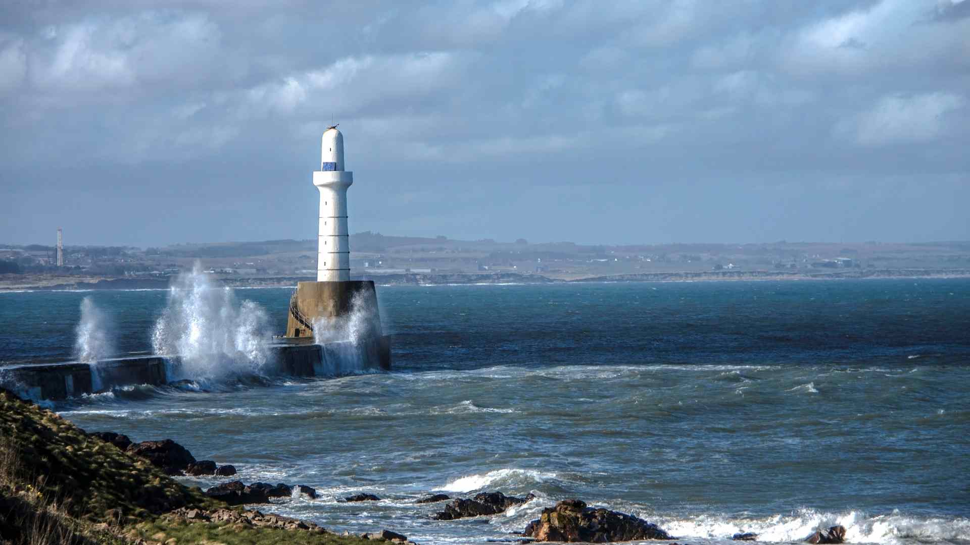 Stone lighthouse facing rough North Sea waves near Aberdeen
