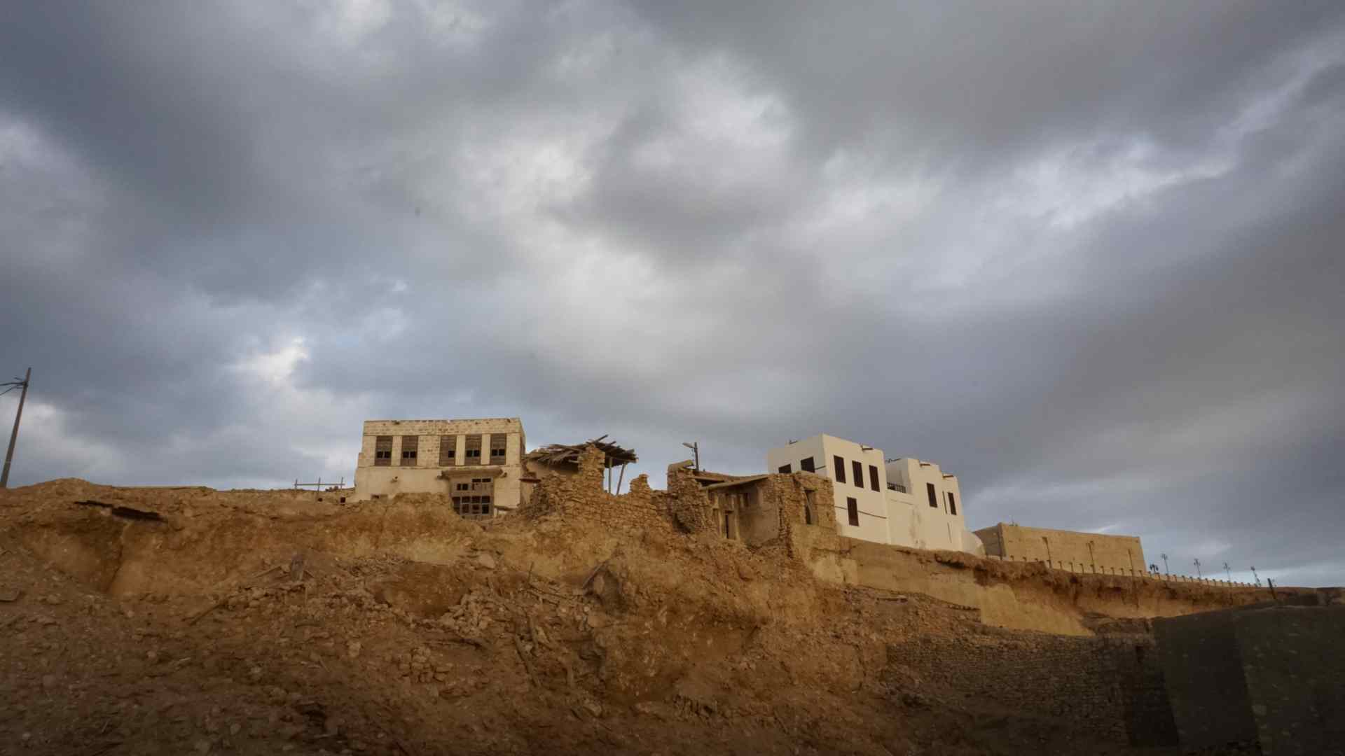 Old stone buildings beneath storm clouds near Al Wajh