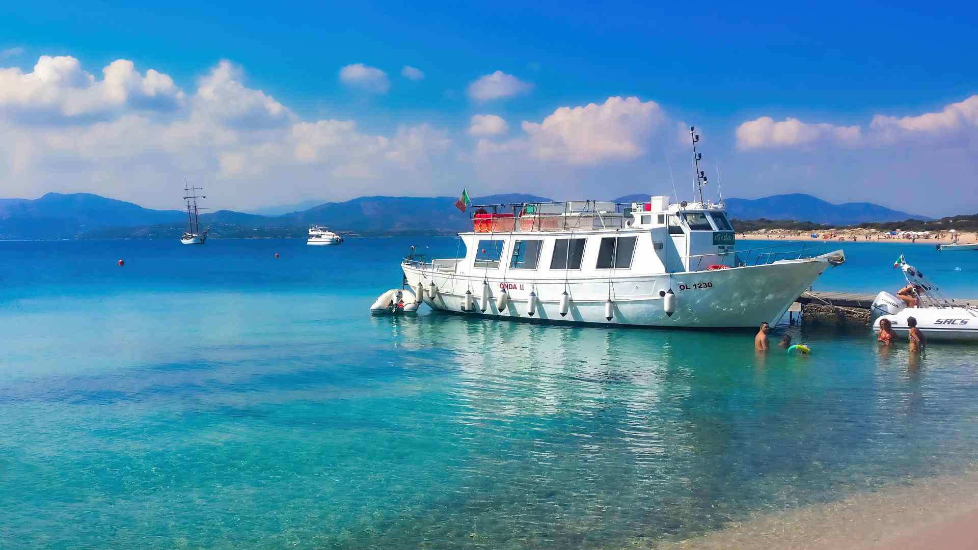Tour boat floating in clear turquoise water near Alghero