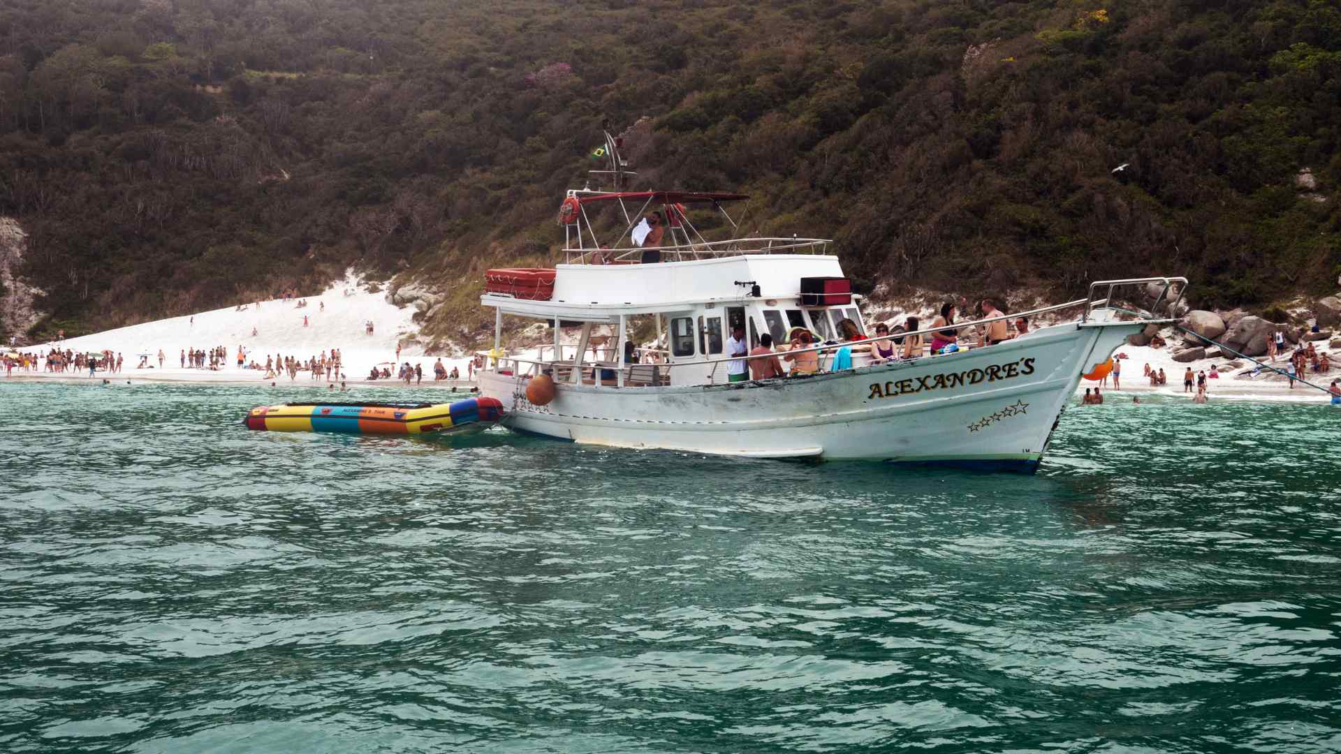 Tour boat anchored beside a crowded white sand beach