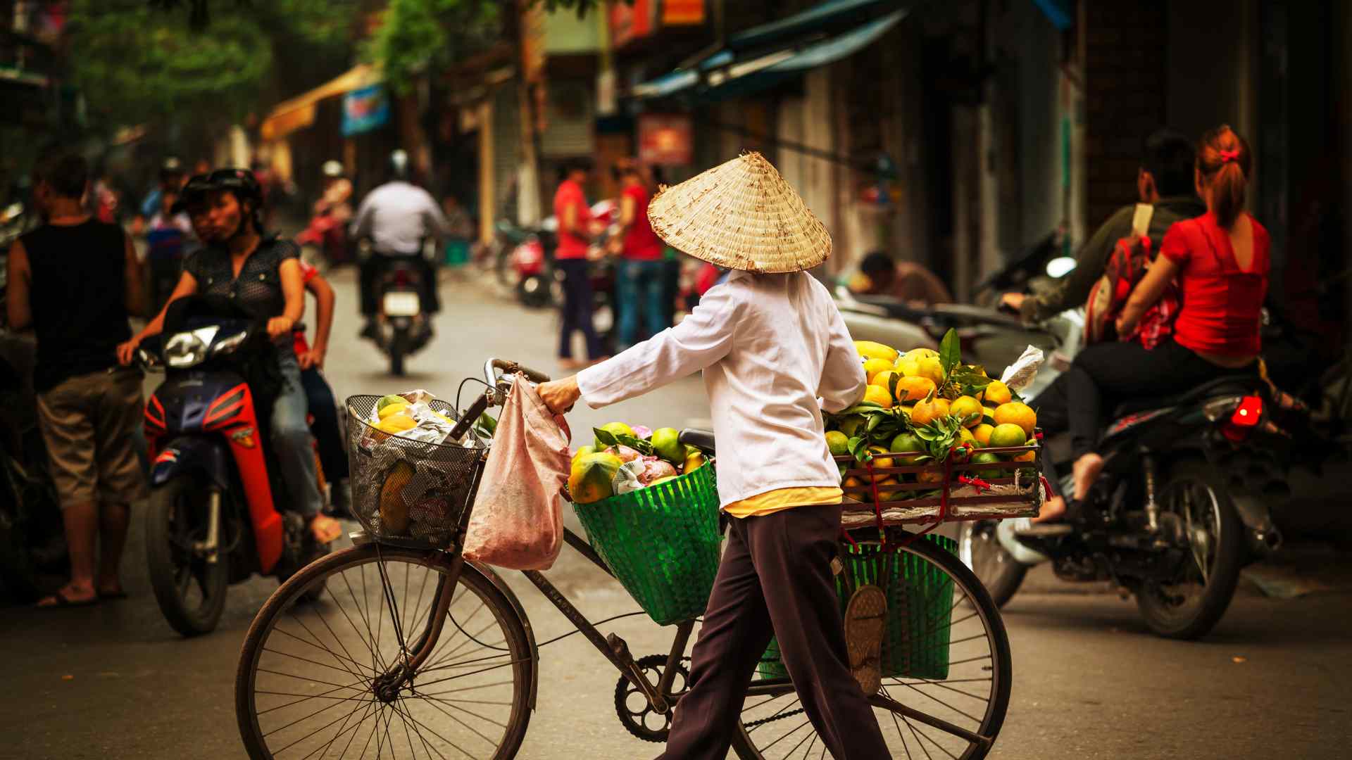 Vietnamese street vendor pushing a bicycle through city traffic