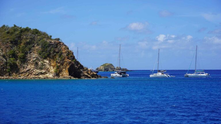 Dark blue water with 3 sail boats by a tall piece of land
