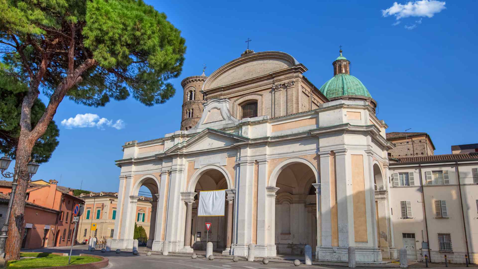 Historic basilica facade beneath a pine tree in Ravenna