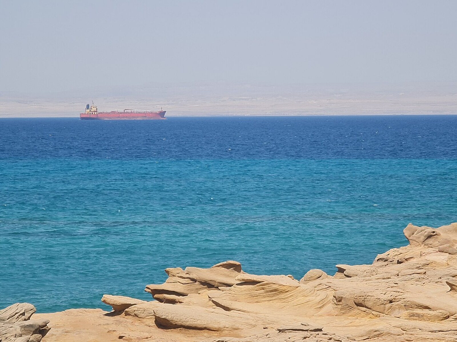 Turquoise Red Sea water and rocky shoreline at Ain Sokhna, Egypt, with a ship in the distance