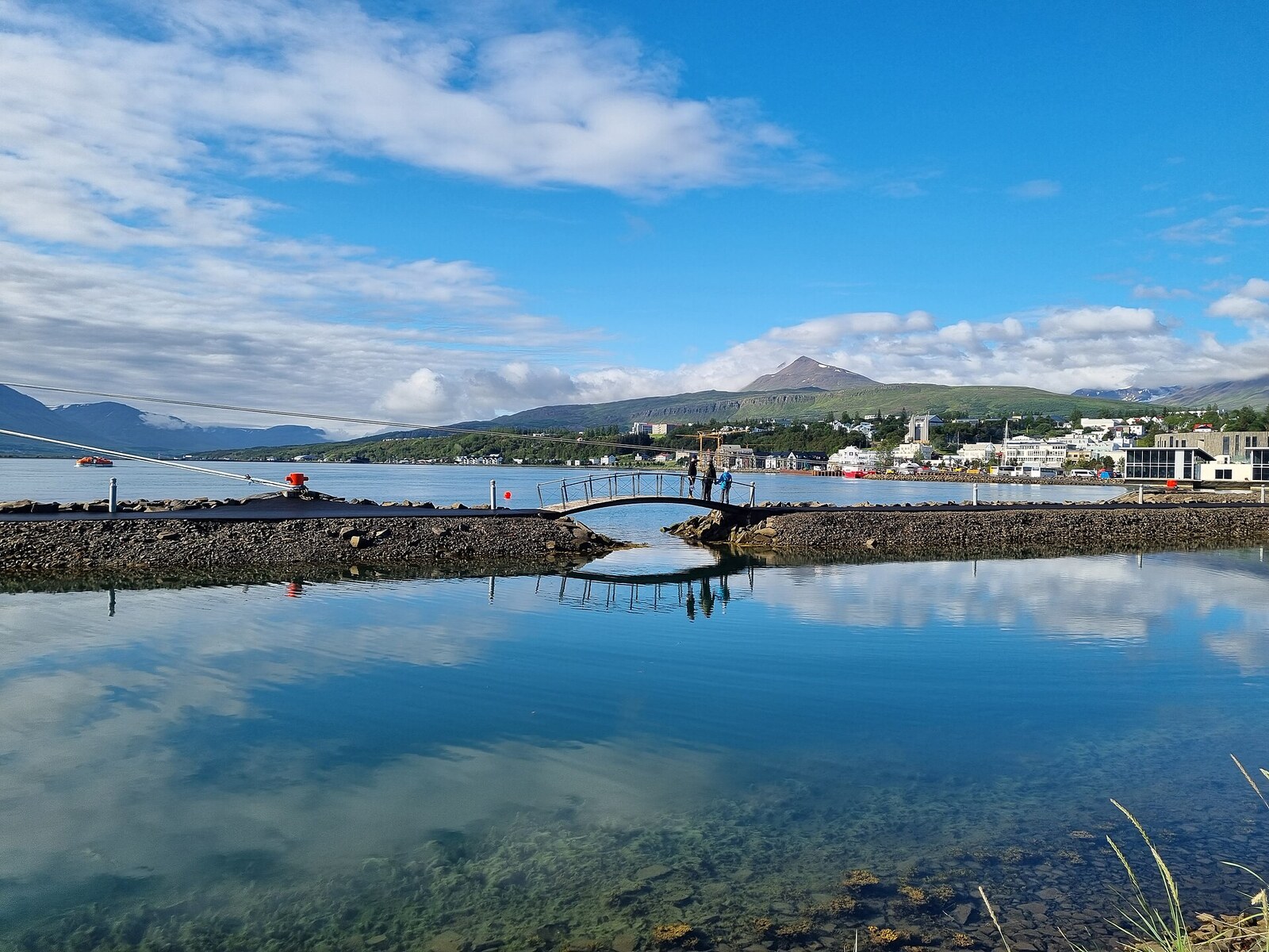 Calm reflective water along the Akureyri waterfront with the city and mountains beyond