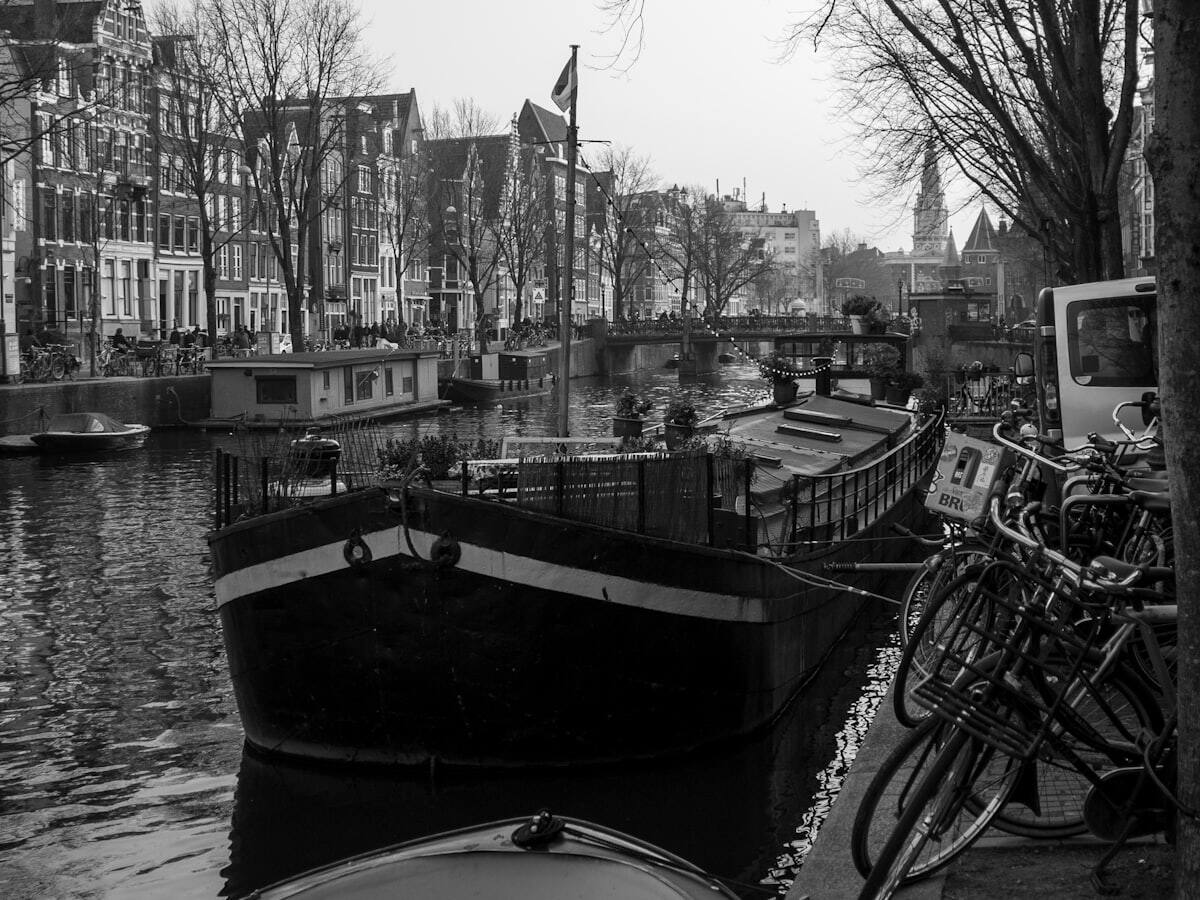 Boats moored along an Amsterdam canal beside historic houses and bicycles