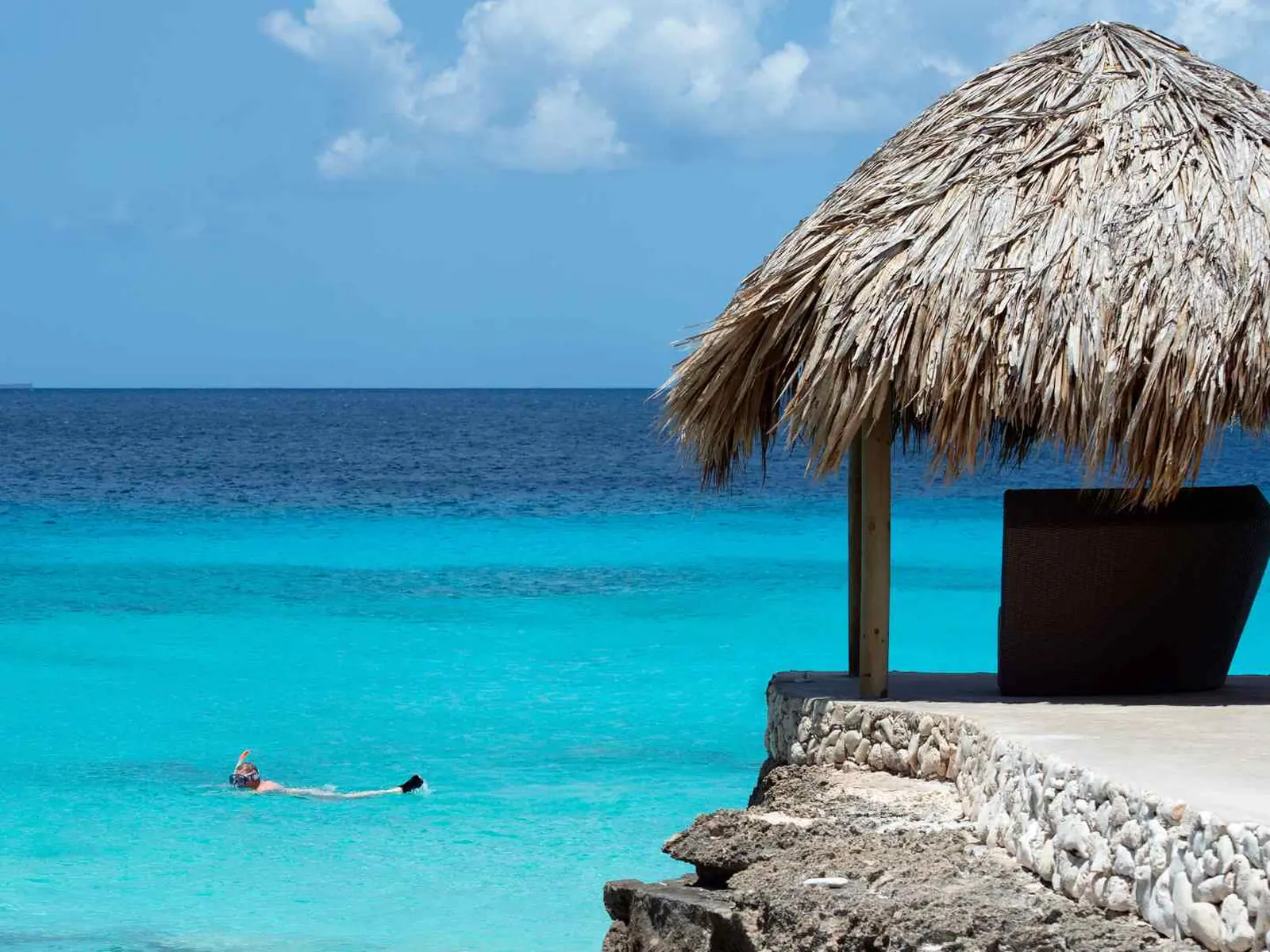 Swimmer in turquoise water beside a thatched beach shelter in Bonaire
