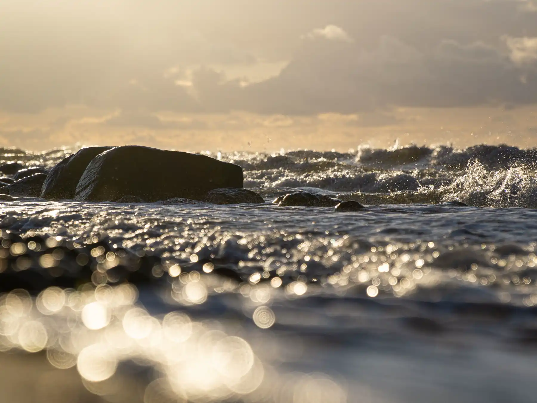 Sunlit waves breaking over rocks along the Baltic Sea coast near Warnemünde.