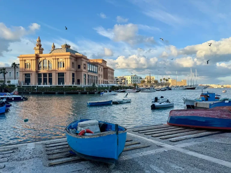 Boats in Bari Harbor beside a historic waterfront building under blue skies.