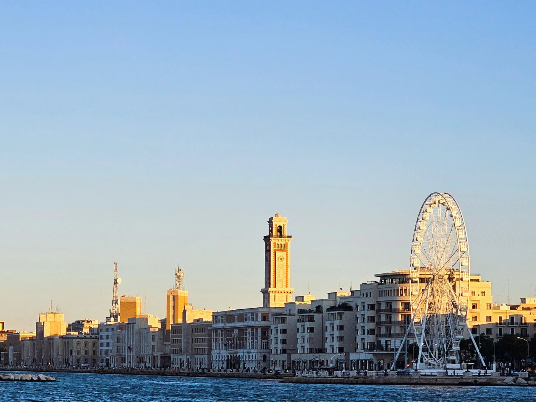 Bari's waterfront skyline and Ferris wheel in warm sunset light.