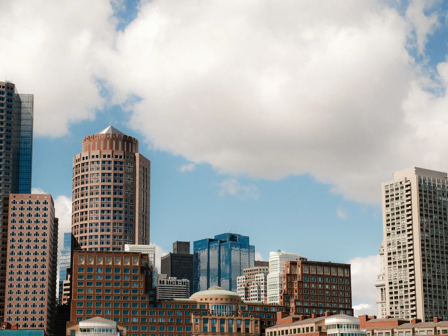 Boston waterfront buildings beneath large clouds and a blue sky.