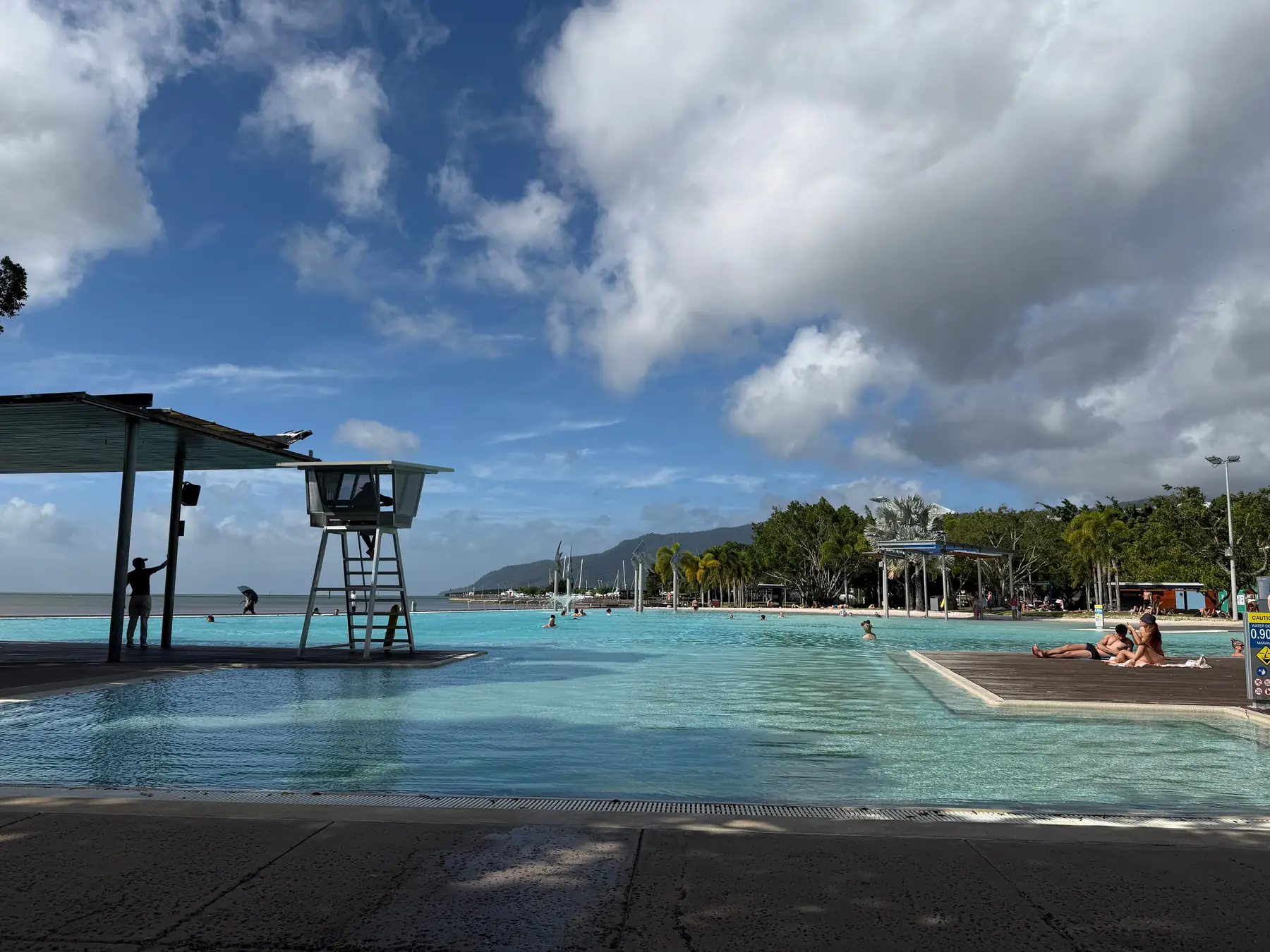 Cairns Esplanade Lagoon with palm trees and the city waterfront under blue skies.