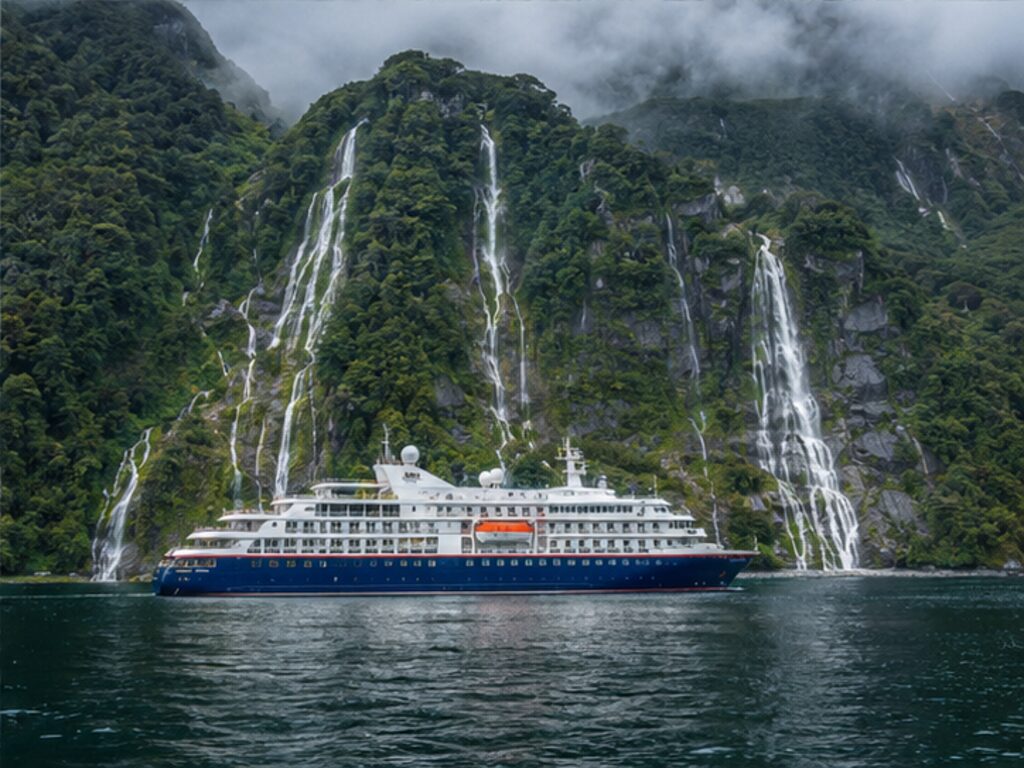 Passenger ship beneath waterfalls and forested cliffs in the Chilean fjords
