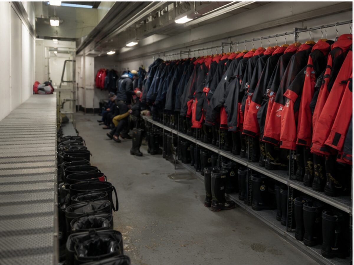 Organized expedition ship mudroom with rows of boots and weatherproof jackets