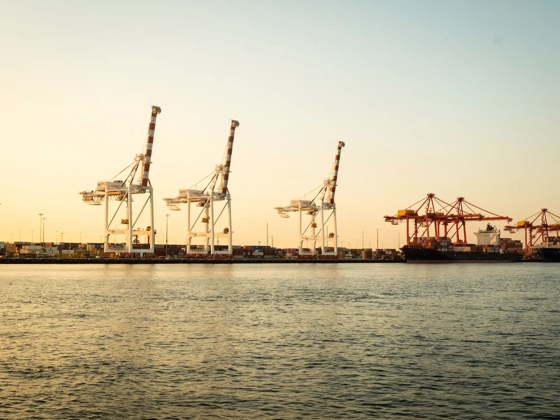 Ships and cargo cranes at Fremantle Port beneath a colorful sunset sky.