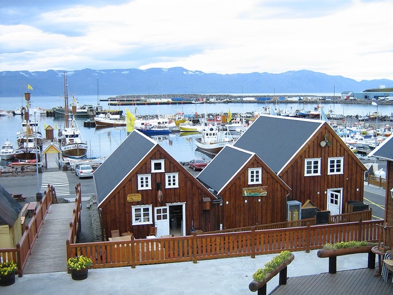 Wooden harbor buildings and boats in Húsavík, Iceland, with mountains across the bay