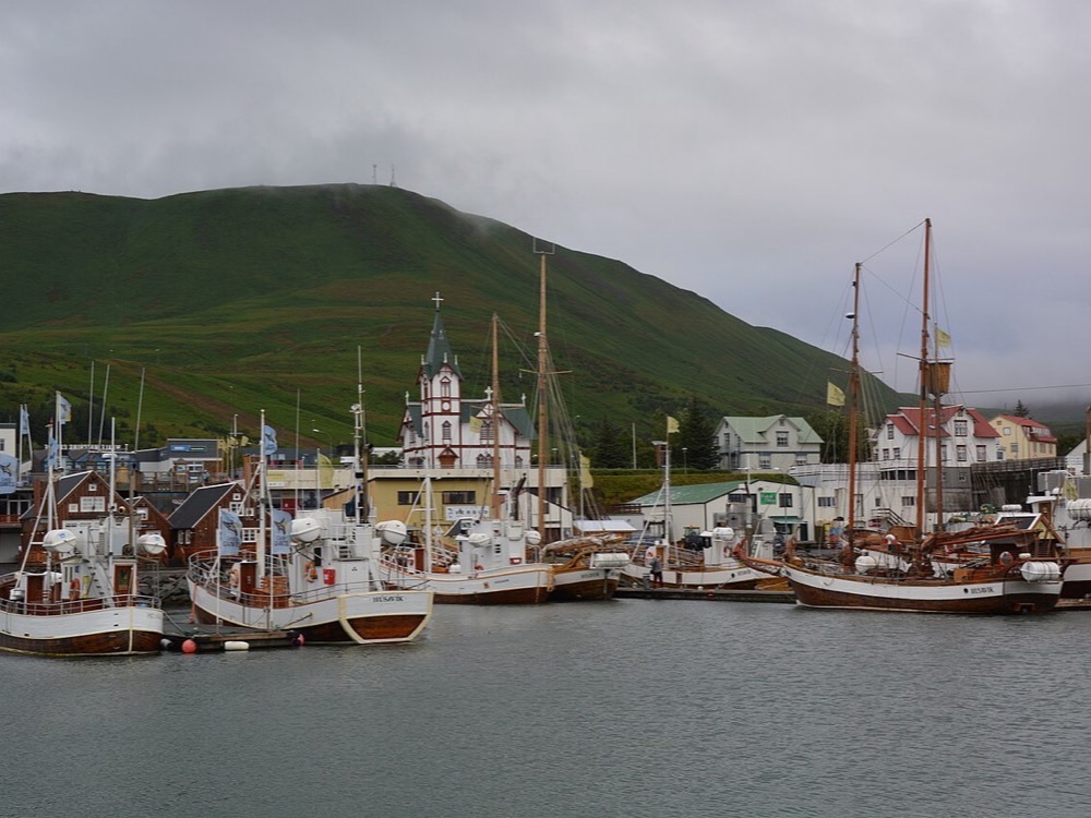 Traditional boats moored in Húsavík harbour beneath the town church and green hills