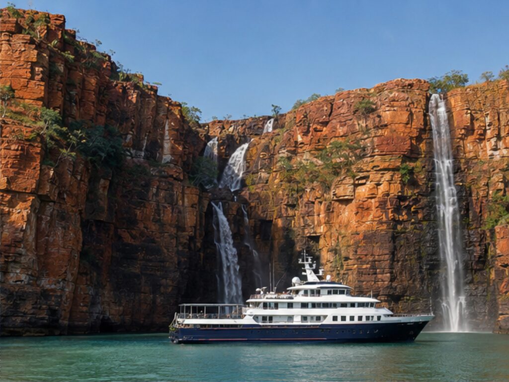 Small expedition vessel beneath red cliffs and waterfalls on Australia's Kimberley coast