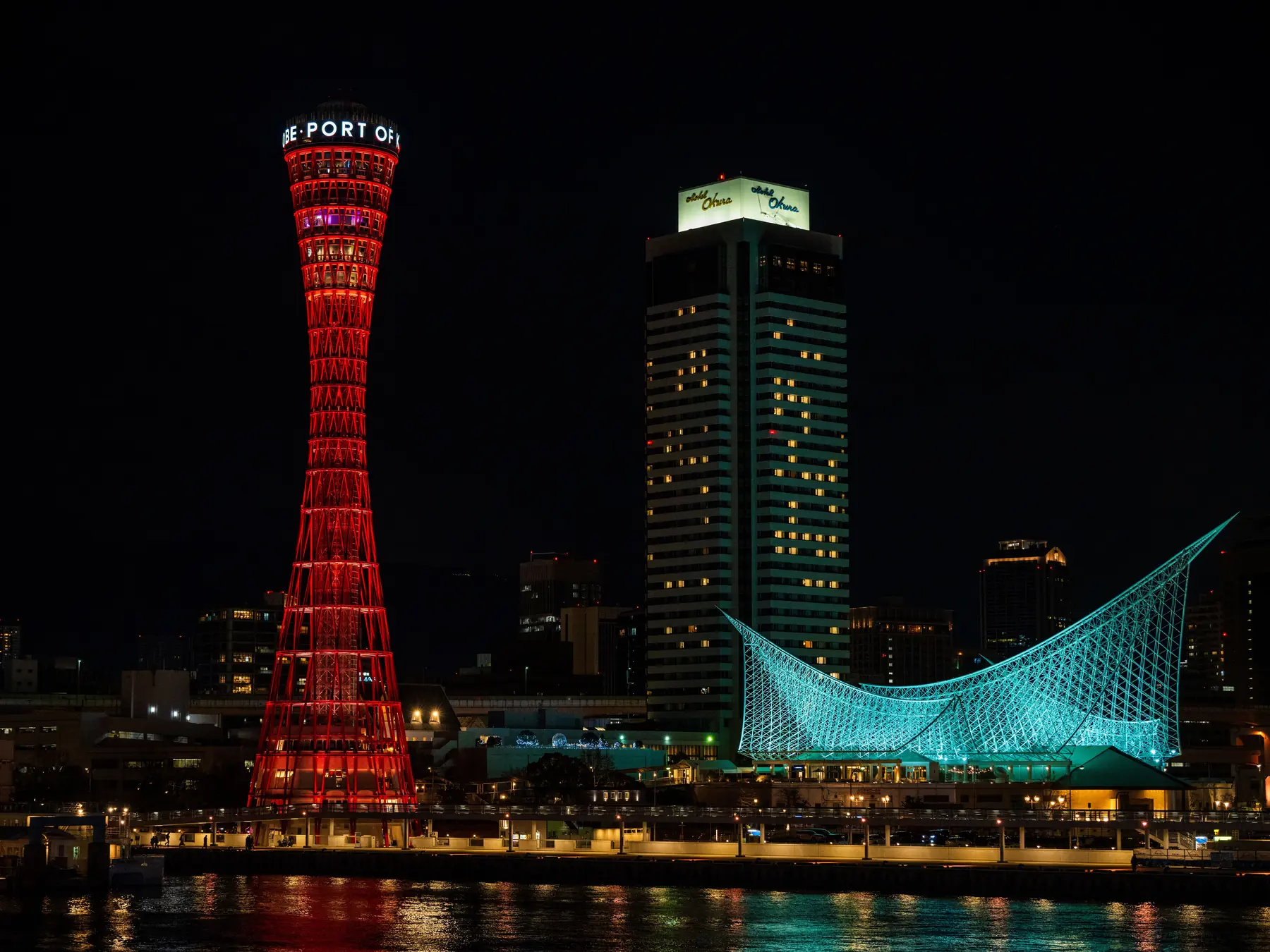 Kobe Port Tower and Maritime Museum illuminated and reflected in the harbor at night.