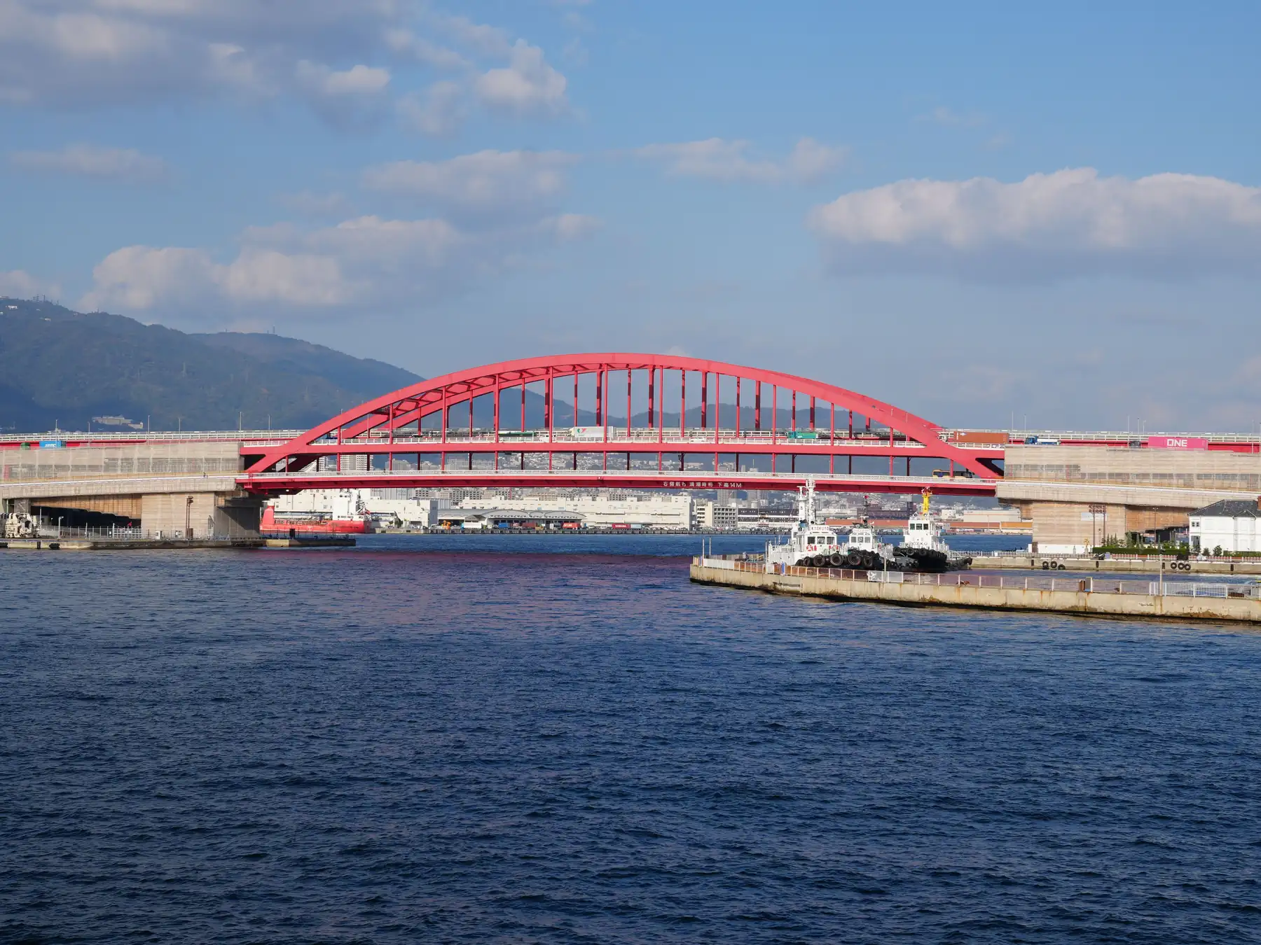 A bright red bridge spanning Kobe Port under a clear blue sky.